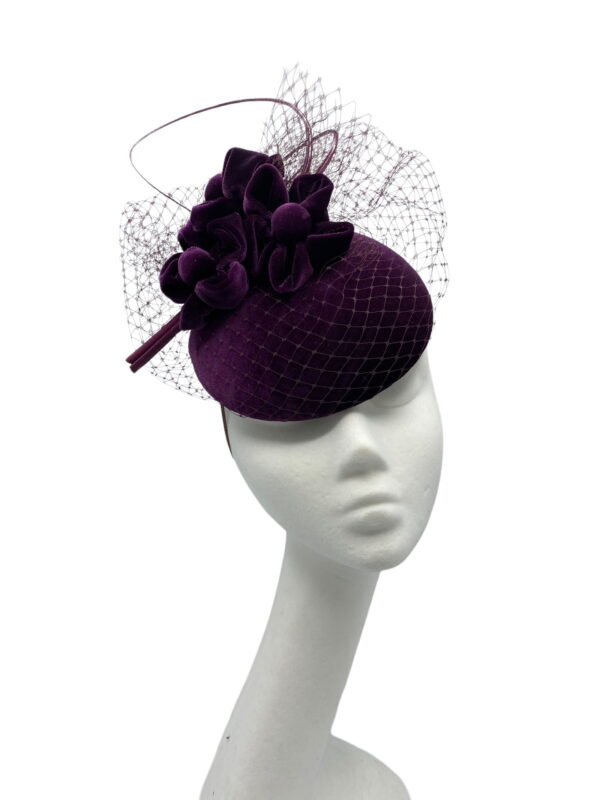 Purple velvet headpiece with veiled detail and finished with a curled quill.